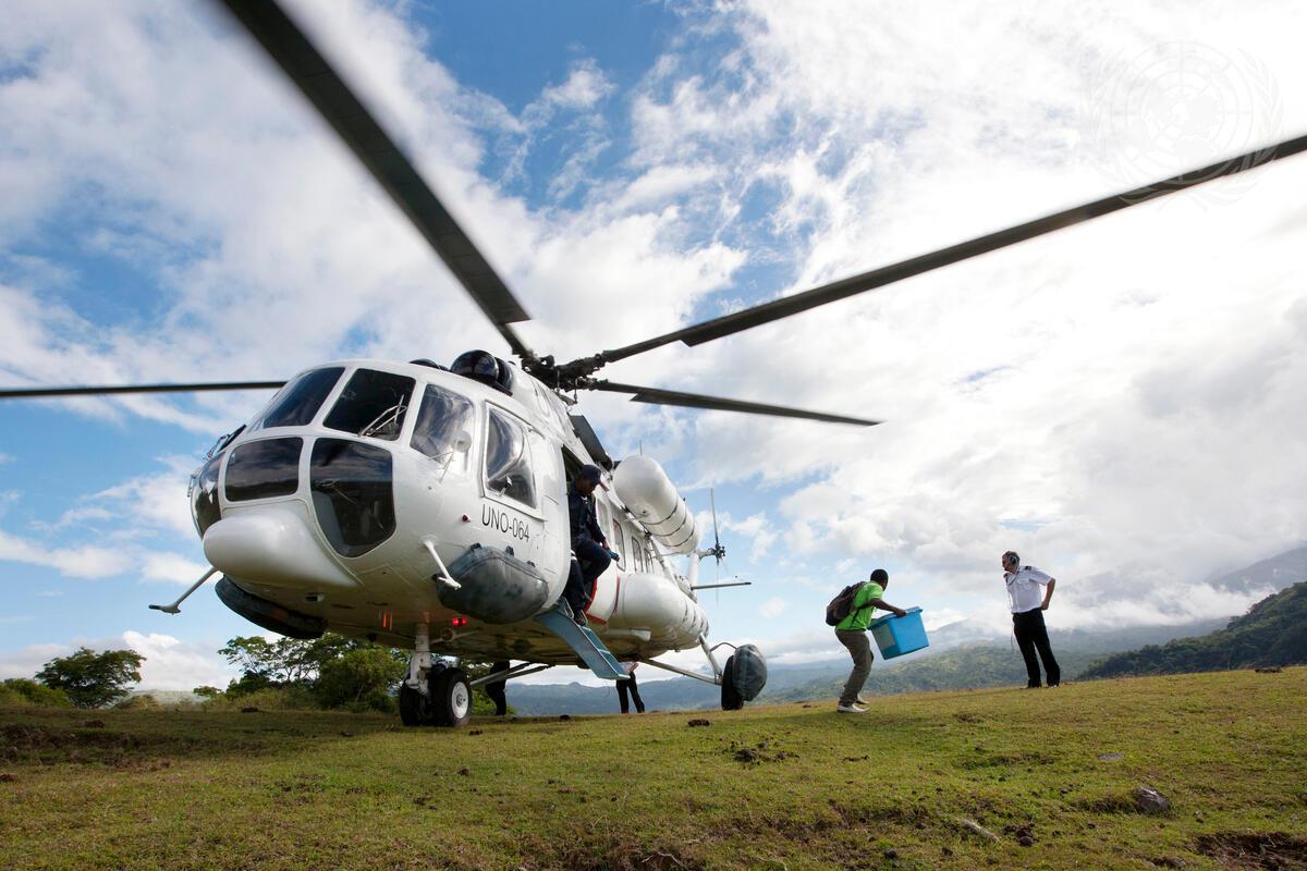 A helicopter with a person walking away from the open door holding a blue box.