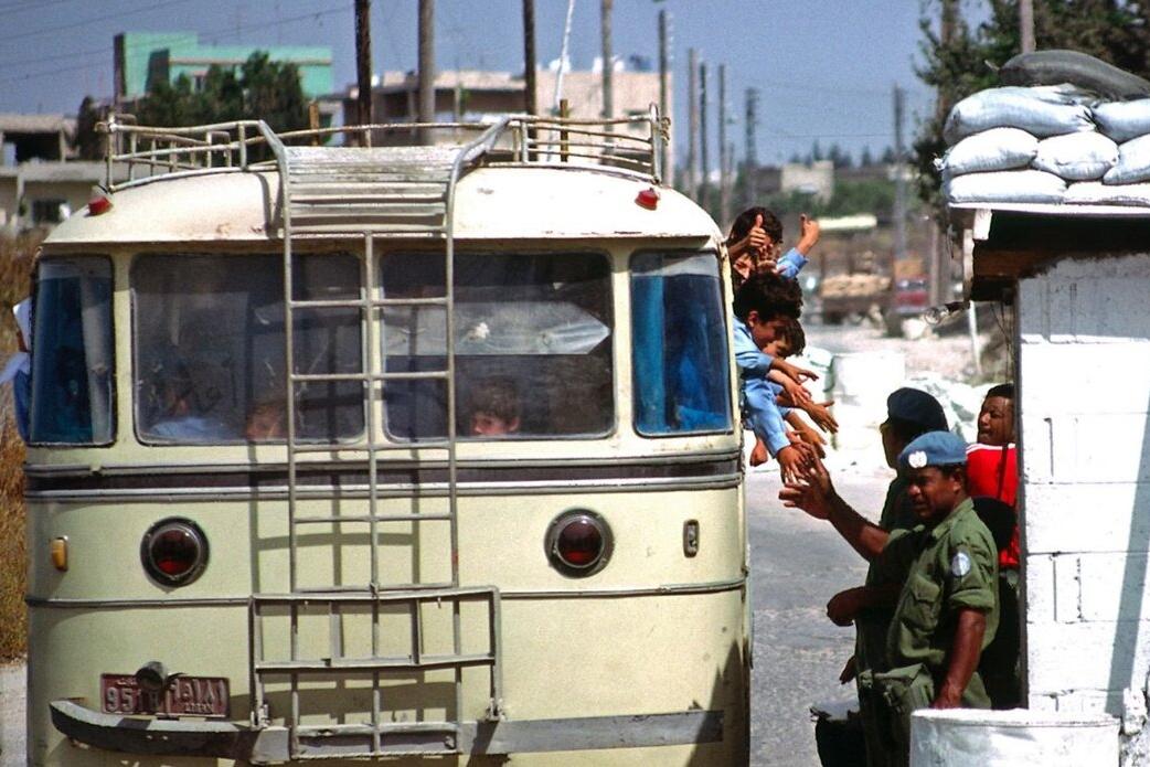 Children reach out to peacekeepers from inside of a vehicle.